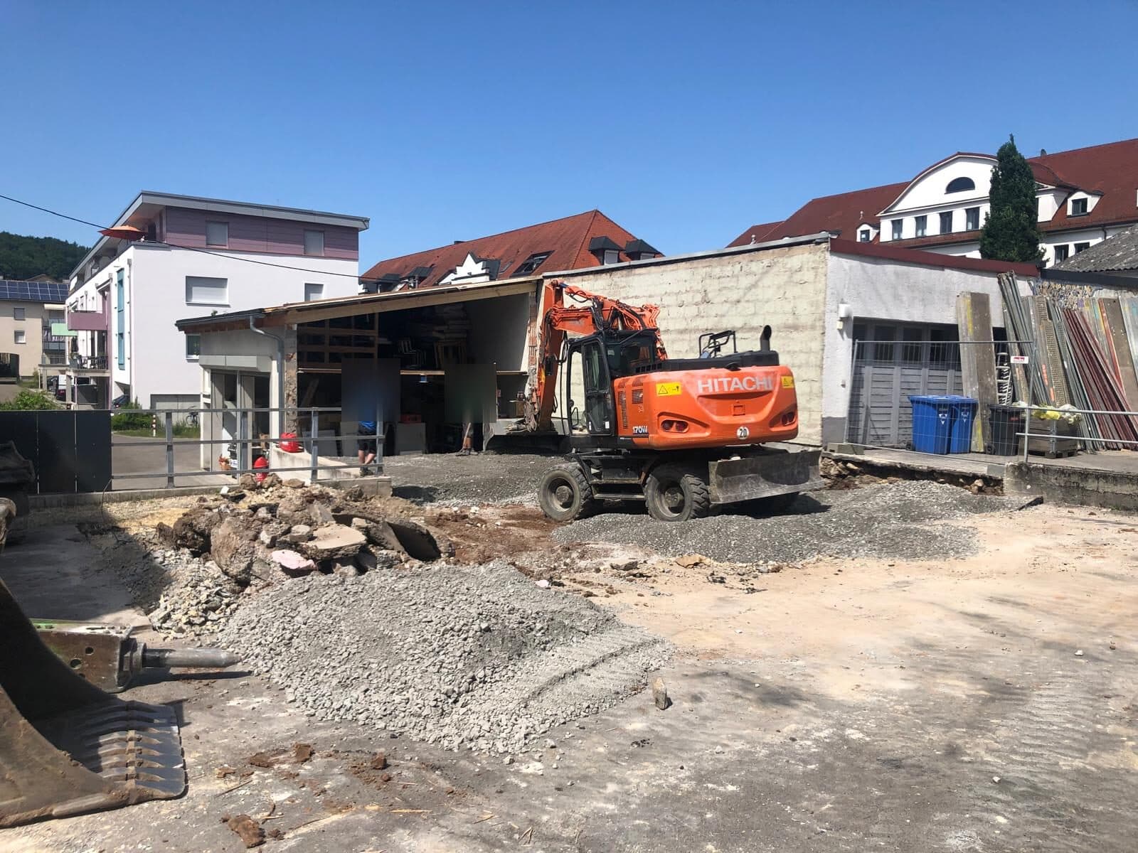 Ein Bagger auf dem geräumten Grundstück, daneben Schutthaufen und die Reste des alten Gebäudes