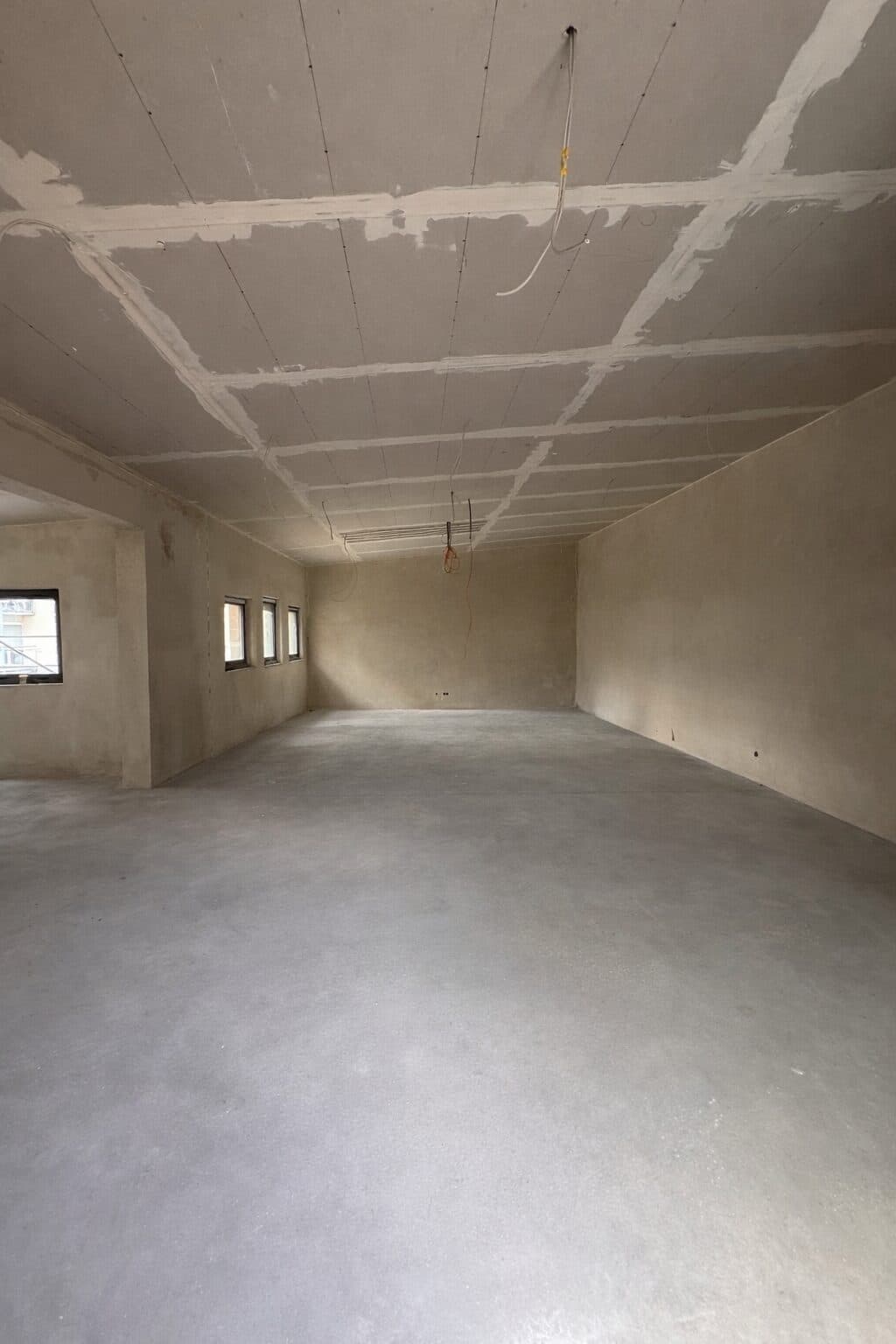 Der große Saal im Rohbau: Betonboden, verspachtelte Decke aus Gipskarton, kleine Fenster an der Seite